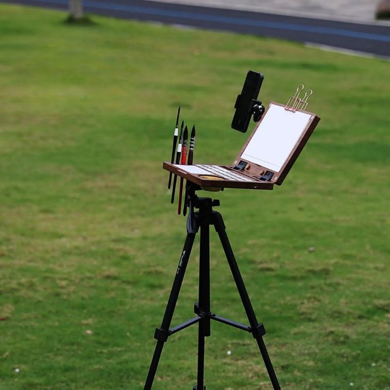 Walnut art kit mounted on a black tripod on grass with brushes and a phone holder set up outdoors