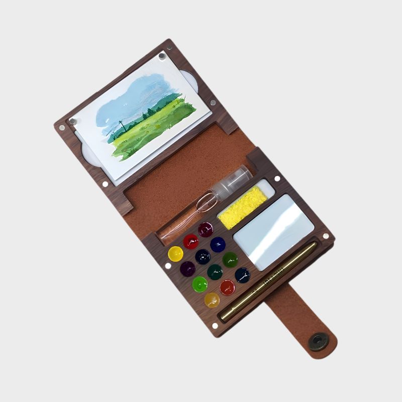 Portable art set with watercolors, brushes, and a small painting on a white background