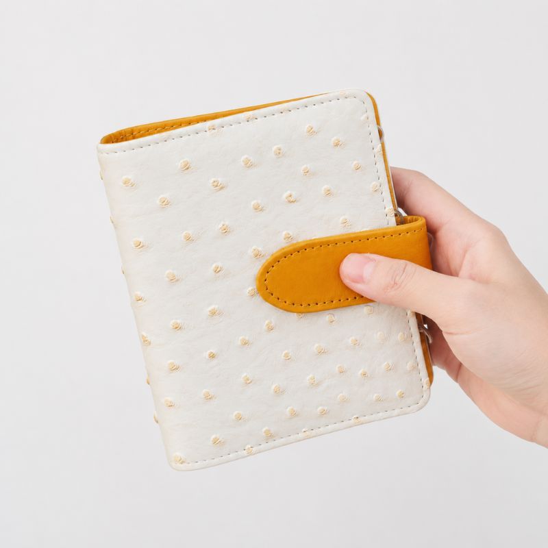 Closed cream Mango Pudding ostrich-texture Nomad kit with orange snap tab held in hand